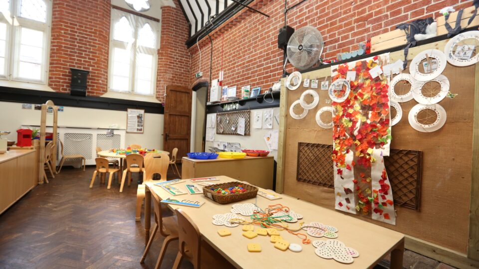 Purbrook nursery classroom with wooden tables, autumn crafts, and educational materials beneath high arched windows.