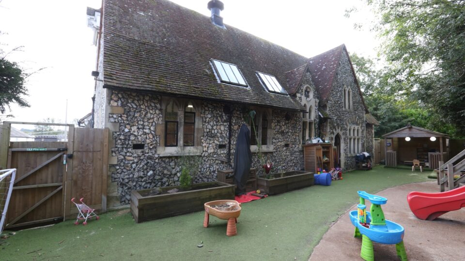 Outdoor play area of a pre-school in Purbrook, featuring a historic stone building with toys and activity stations.