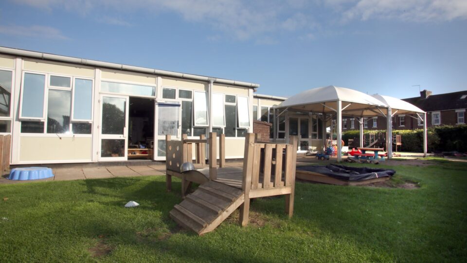 Outdoor play area at a day nursery in Shoreham, featuring wooden play equipment and a covered play space.