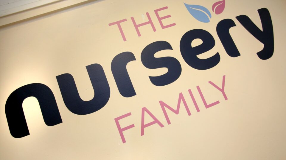 Wall sign reading "The Nursery Family" in bold letters with blue and pink leaf designs.