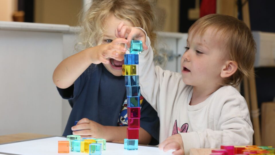 Two children excitedly build a tall tower using colourful translucent blocks during playtime.