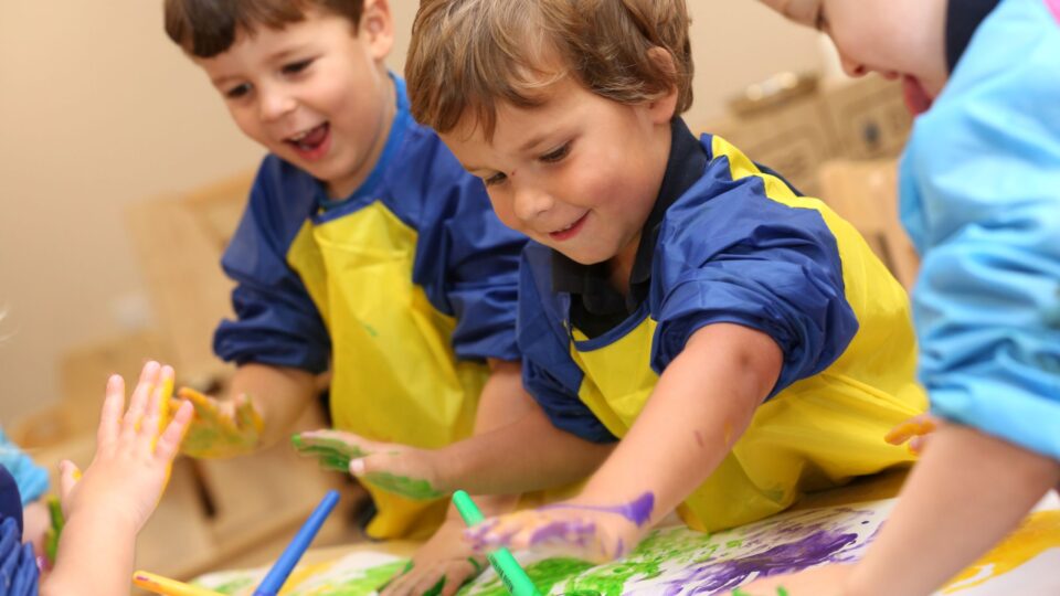 Children at a pre-school in Southwater enjoying finger painting, wearing colourful aprons and smiling as they create art.